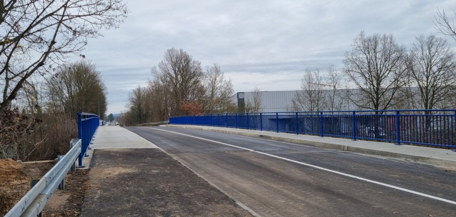 View of the newly renovated Haingrabenstraße bridge with blue railings and asphalt carriageway under a cloudy sky.