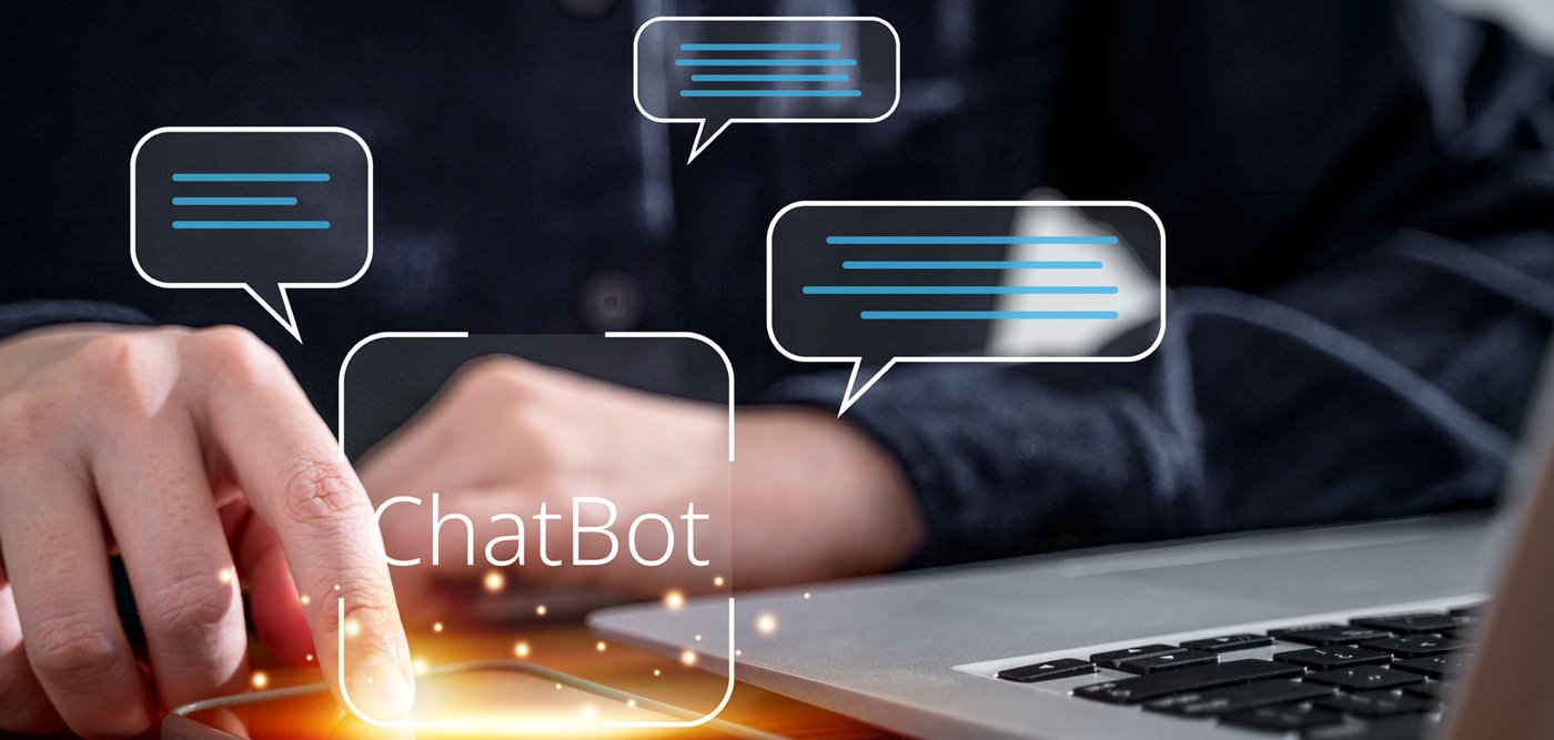 Chatbot choice A hand taps on a smartphone, a laptop can be seen next to it. A speech bubble with the term "chatbot" can be seen virtually.