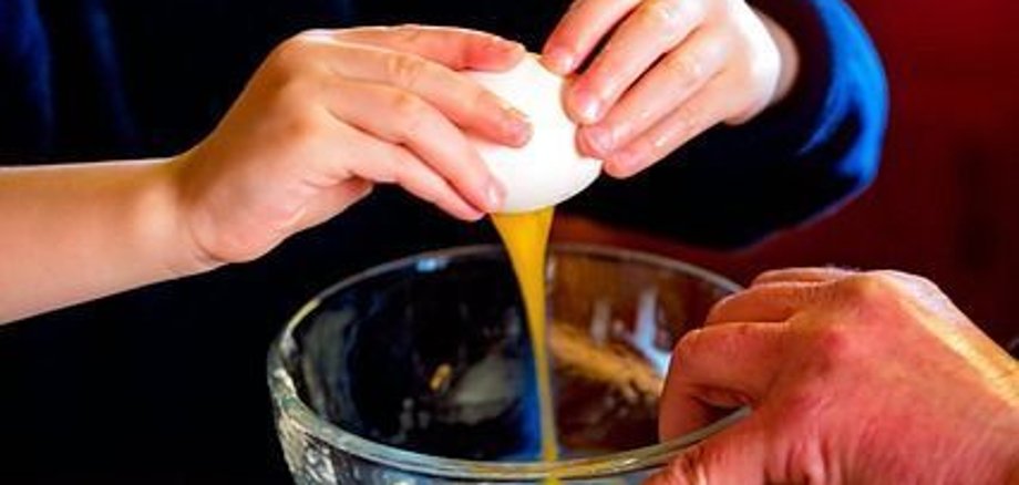 A child breaks an egg and puts the yolk and white into a glass bowl.