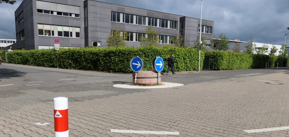 Small roundabout between Kita 18 and Georg Büchner School Small roundabout with two blue directional arrows on a round central island platform between Kita 18 and Georg Büchner School, surrounded by paved ground and the school's multi-storey building in the background