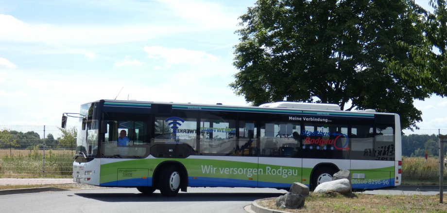 City bus on route OF-40 in Rodgau with the inscription 'Wir versorgen Rodgau' (We supply Rodgau) travelling on a road with trees and rocks at the side