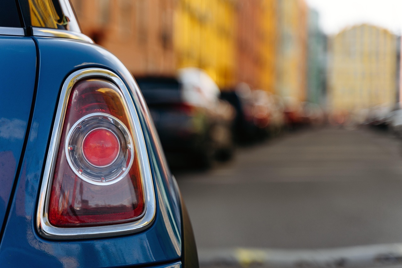 In the foreground you can see the tail light of a car, in the background a street canyon with houses in front of which many cars are parked.