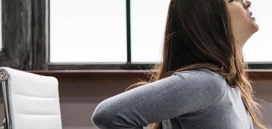 Two women in sportswear. The woman on the left is wearing a black T-shirt and leggings with a purple pattern. The woman on the right is wearing a black top and black leggings, with pink shoes. The woman on the left is supporting the woman on the right, who is standing in a sporty pose.