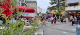 People sit in front of the ice cream parlour on Puiseauxplatz. There are plants in the foreground and passers-by to the side.