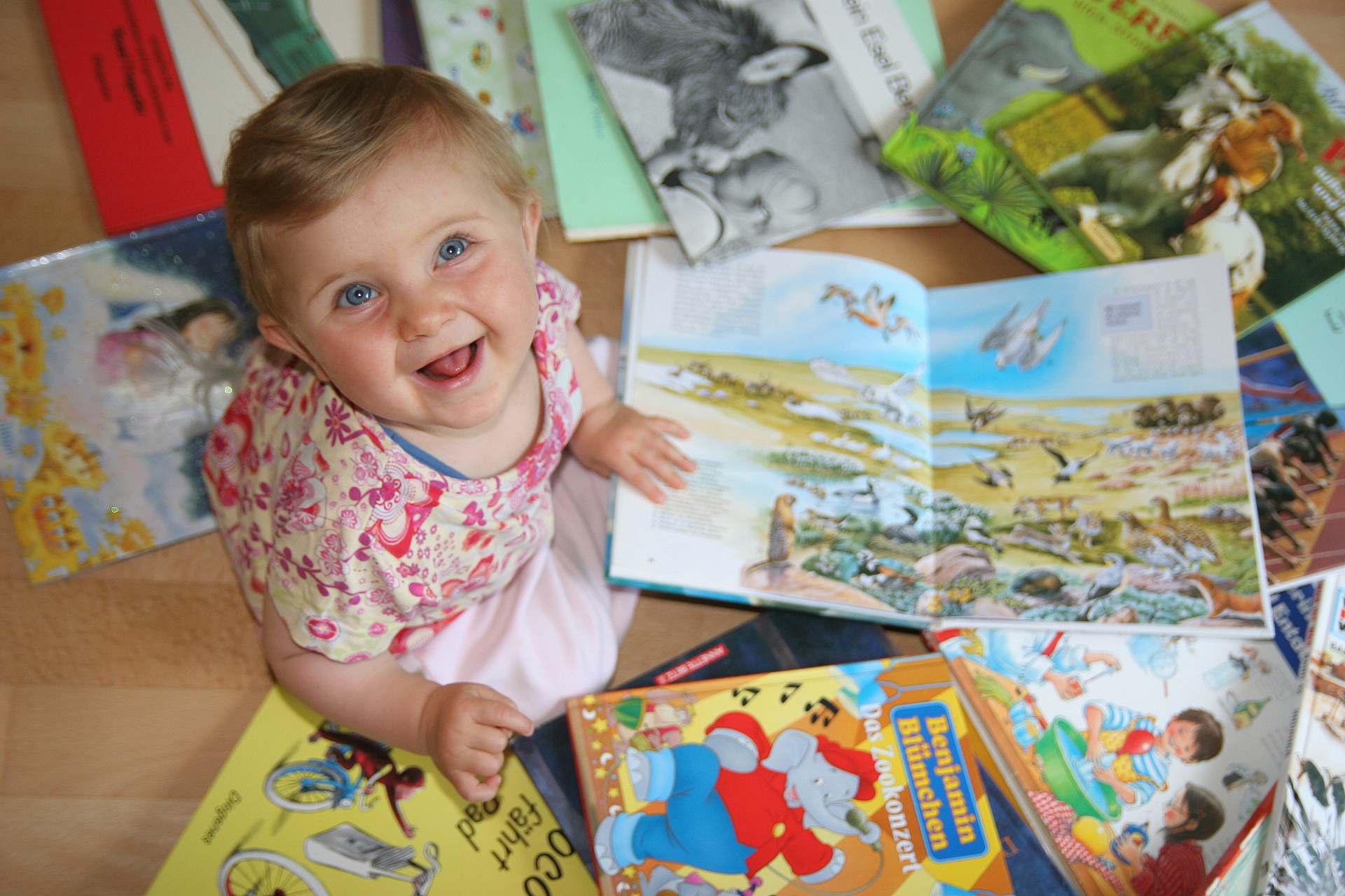 Infant Small child sits on the floor and looks at several open children's books with colourful illustrations