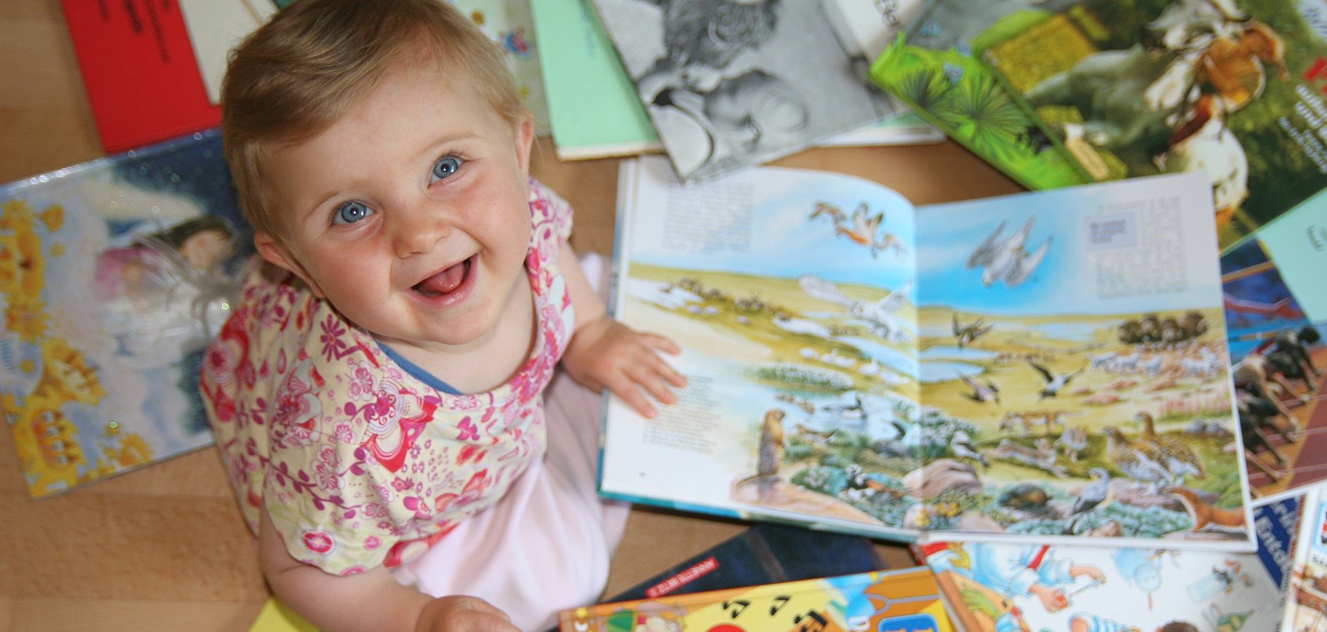 Infant Small child sits on the floor and looks at several open children's books with colourful illustrations