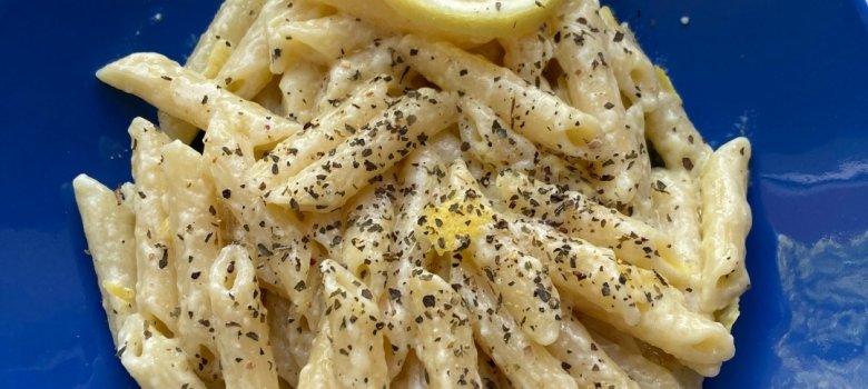 The picture shows a blue plate with pasta, served with a slice of lemon.