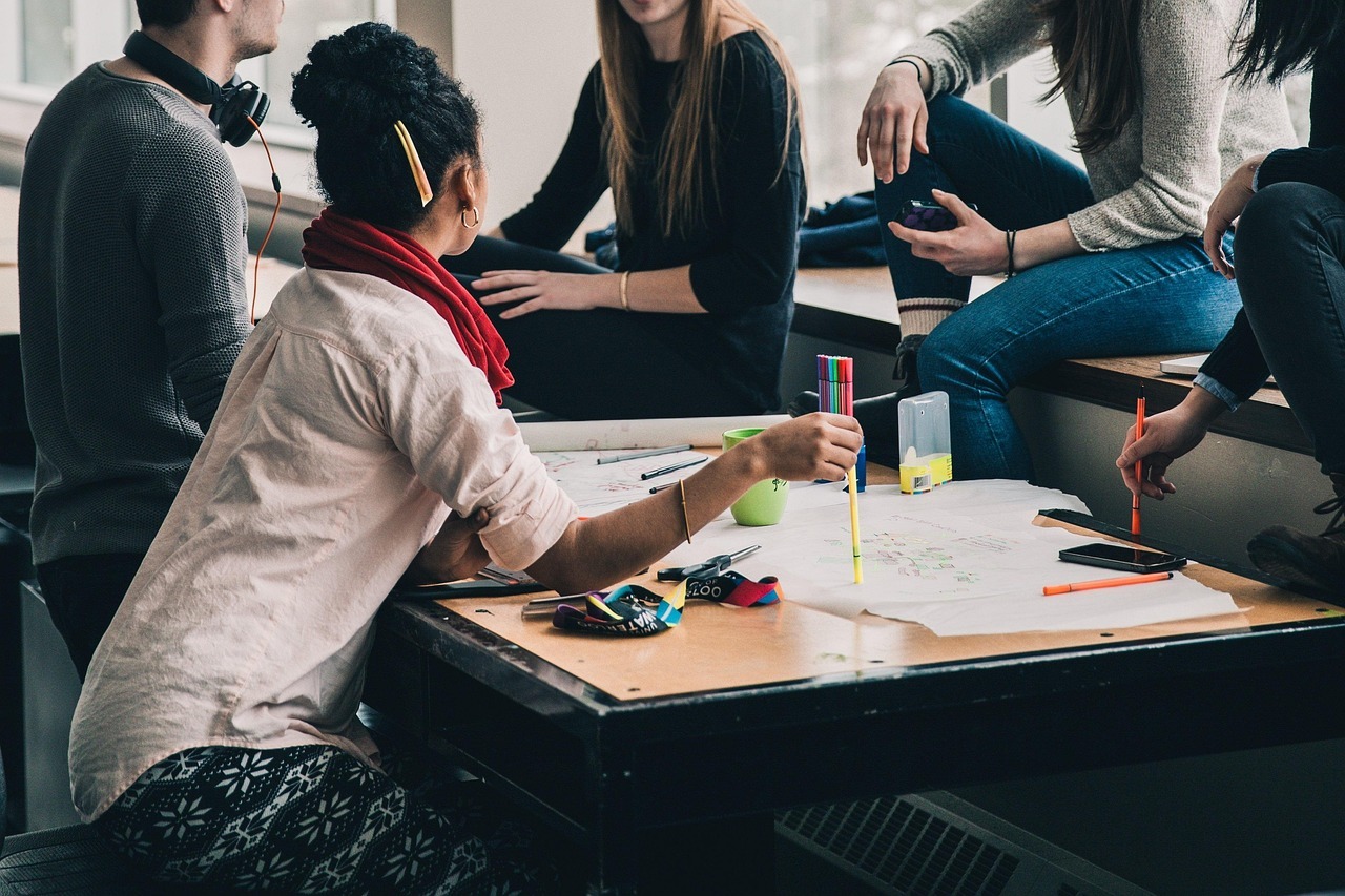 Several young adults sit around a table in the language café, discussing and working together on a large sheet of paper with pens and markers