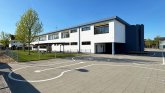 Modern school building with a large schoolyard or forecourt, also a large lawn with a tree in front of the school building