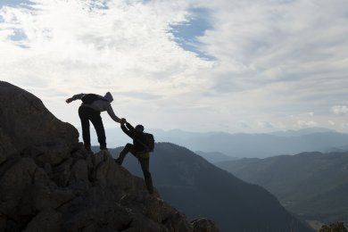 One person helps another to climb a rock in the mountains
