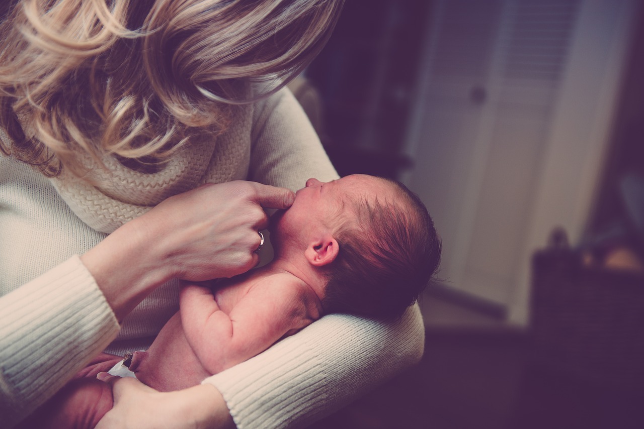 A woman lovingly holds a newborn baby in her arms. The scene is warm, calm and protective