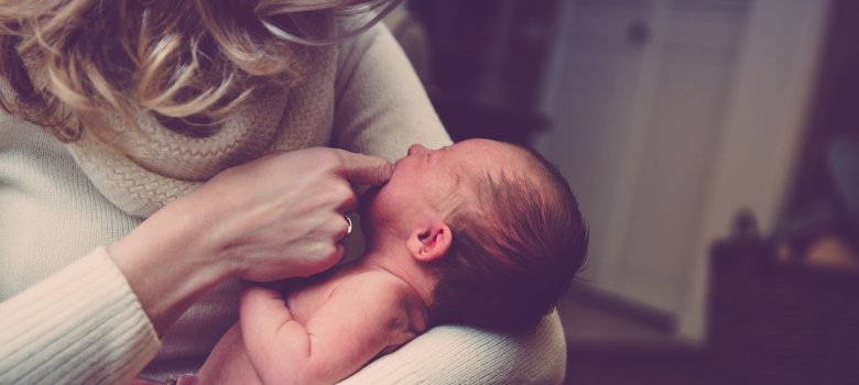 A woman lovingly holds a newborn baby in her arms. The scene is warm, calm and protective