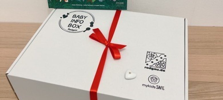 White baby info box with red ribbon and book White baby info box with red ribbon and book 'Leon's animal cold' with animal illustrations in the background