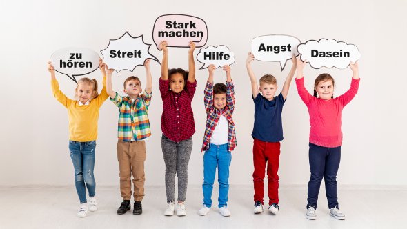 Six children stand next to each other and hold up signs with the words 'to listen', 'fight', 'make strong', 'help', 'fear' and 'existence'