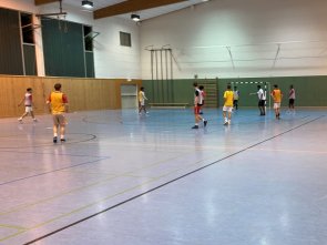 Young people play indoor football in a sports hall, some sit on the bench and watch