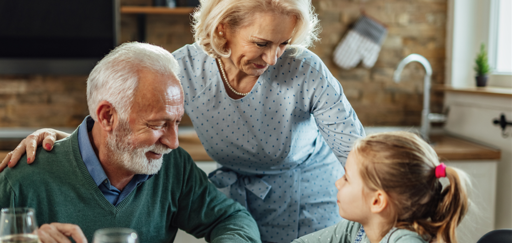 Elderly couple sitting at the dining table, talking to a little girl with a ponytail, table set with salad and drinks