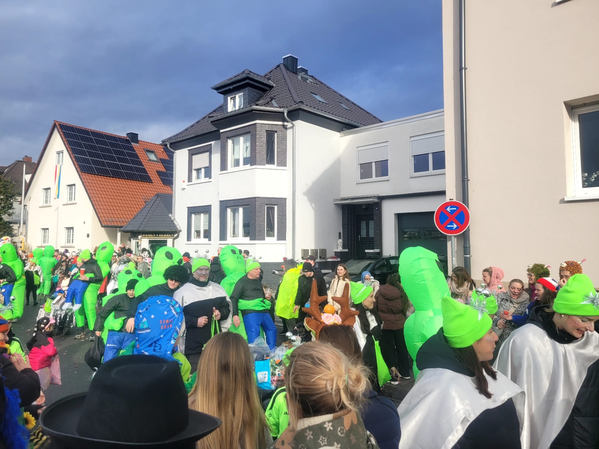 Group of people in green alien costumes and other colourful disguises at the 2026 street parade in front of residential buildings.