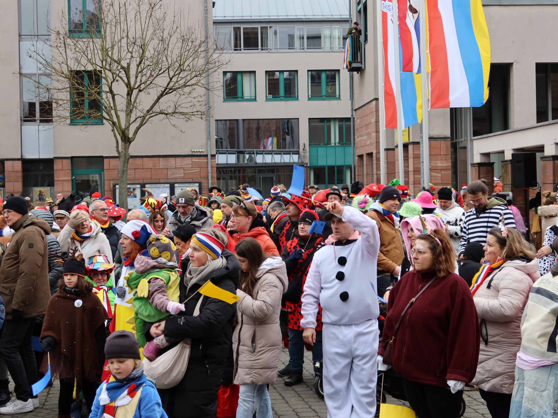 Crowd in colourful costumes at the town hall storm with flagpole and several flags