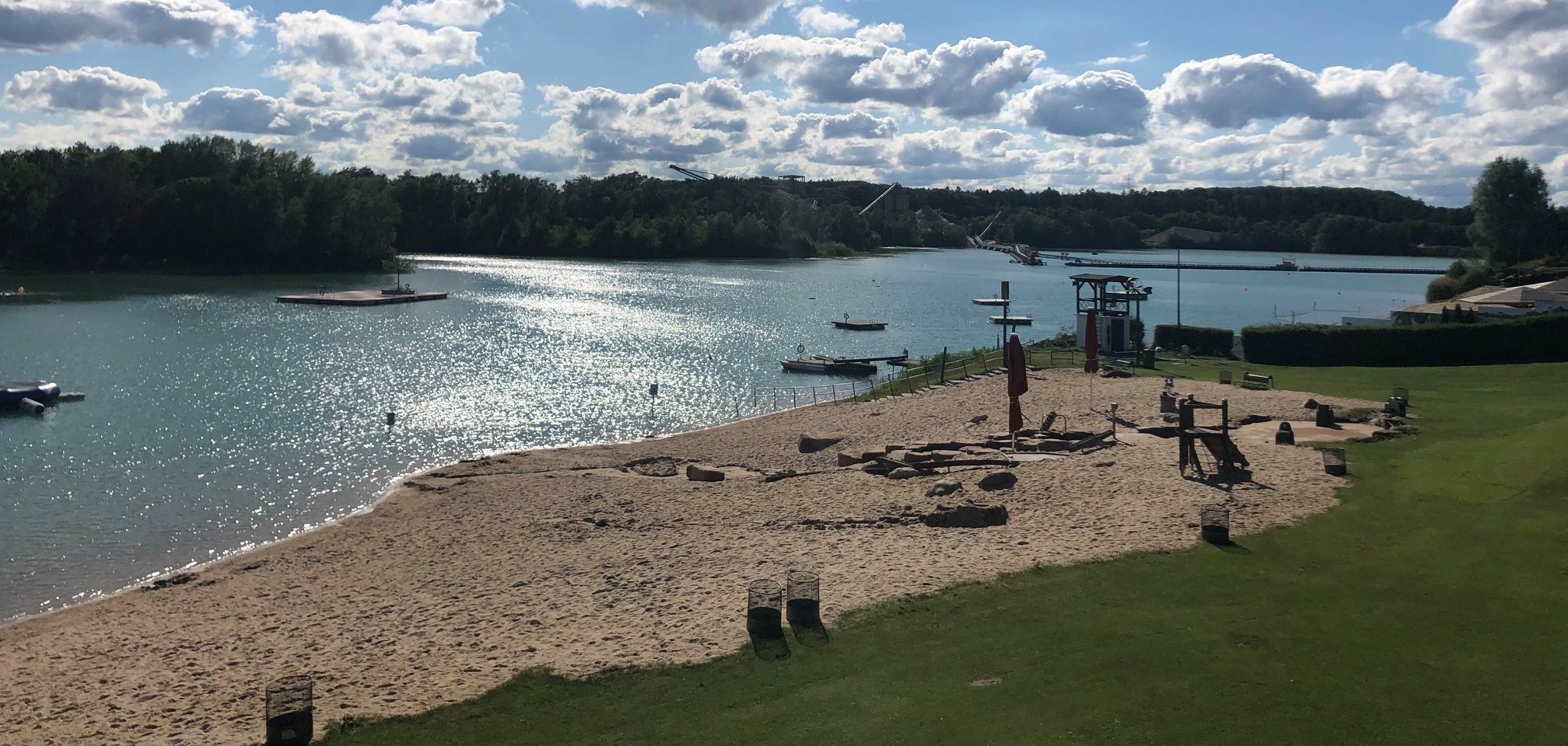 A beach with boats and a lake in the background, surrounded by gentle waves and a green shore.
