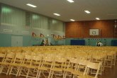Interior view of the Carl-Orff-Schule gymnasium with many wooden chairs in orderly rows.
