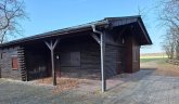 On the left is the wooden building at the Weiskirchen forest leisure centre with a paved forecourt, on the right you can see the field and some forest.