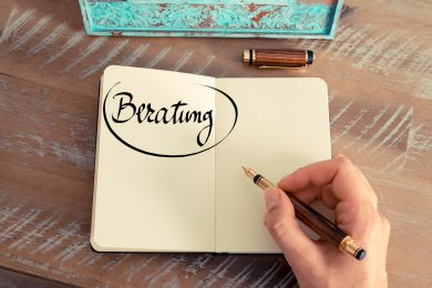 Hand writes the word 'counselling' with a fountain pen in an open notebook on a wooden table.