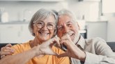 An elderly lady and a gentleman hold their hands together to form a heart.