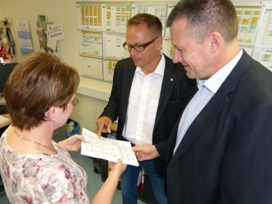 Three people are standing in an office, holding a document and talking about it
