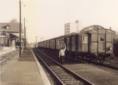 Picture from 1978 with train at Rodgau station, conductor waving, buildings and tracks in the background