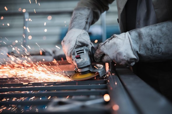 Man wearing protective gloves operates angle grinder, sparks fly when grinding metal.
