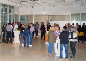 Lots of people are standing around high tables in a large business centre, chatting animatedly.