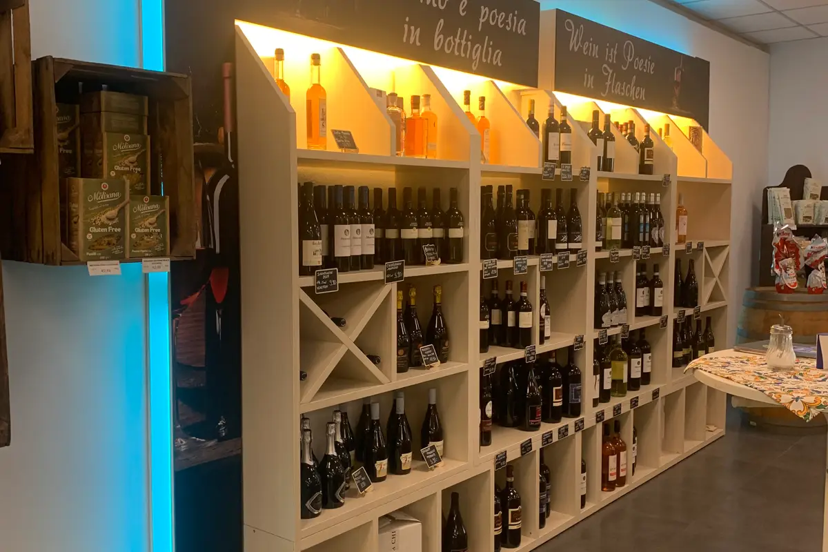 Estante con varias botellas de vino y licores, sobre dos carteles con los textos "El vino es poesía en botella" y "El vino es poesía en bottiglia".