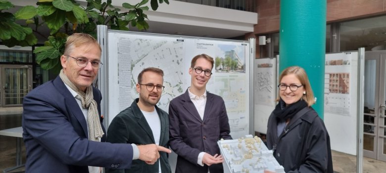 Cuatro personas, de izquierda a derecha Marcus Hille (presidente del jurado), Valentin Martin, Fabian Wieczorek y Pauline Rohländer (de ROHWAREIMSTUDIO) ante los planos arquitectónicos del diseño con el modelo ganador.