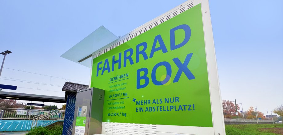 Cartel verde con la inscripción "FAHRRAD BOX" e información sobre precios en los aparcabicicletas de la estación de ferrocarril de Nieder-Roden.