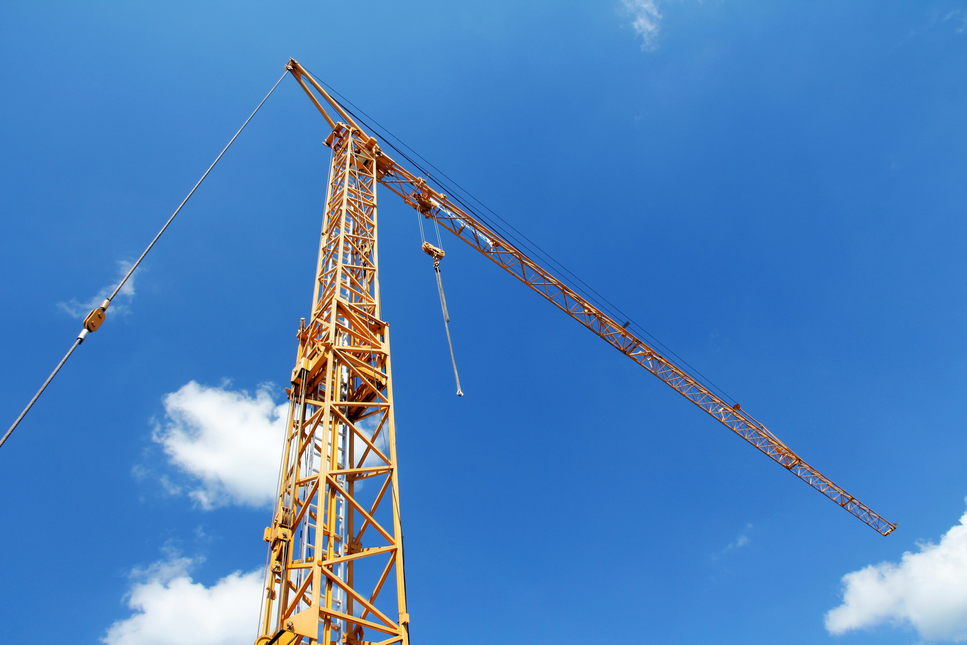 Alta grúa de construcción amarilla frente a un cielo azul con algunas nubes blancas