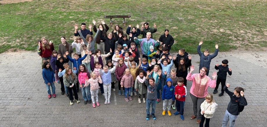 Inauguración de los juegos de las vacaciones de otoño Un grupo de niños y adultos se encuentra en una plaza empedrada y saluda a la cámara