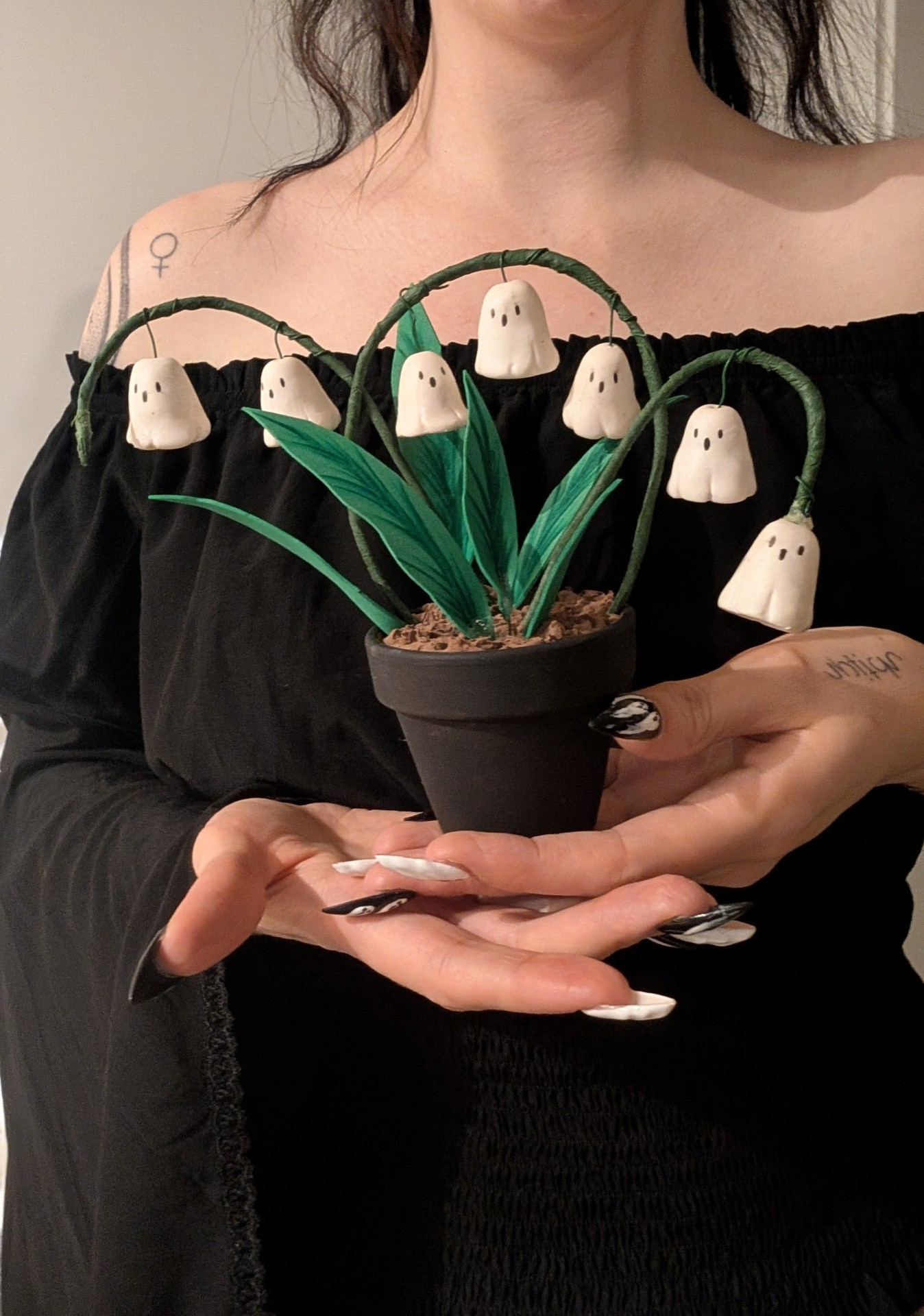 Taller de Halloween Una persona sostiene una pequeña maceta con hojas verdes de las que cuelgan figuras blancas de formas fantasmagóricas que recuerdan a pequeños fantasmas