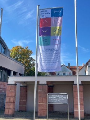 Bandera de la diversidad Bandera de la diversidad con declaraciones sobre la diversidad en Rodgau, entre ellas "Mi Rodgau es...", diversos símbolos y la Declaración de Rodgau sobre la Diversidad en la Bürgermeister-Hermann-Sahm-Platz
