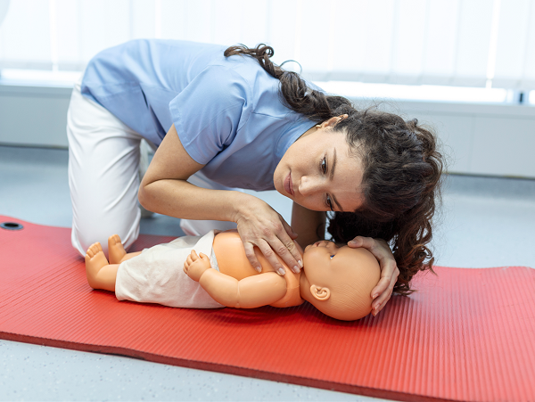 Una persona realiza la respiración boca a boca a un muñeco bebé en una colchoneta roja en un curso de primeros auxilios