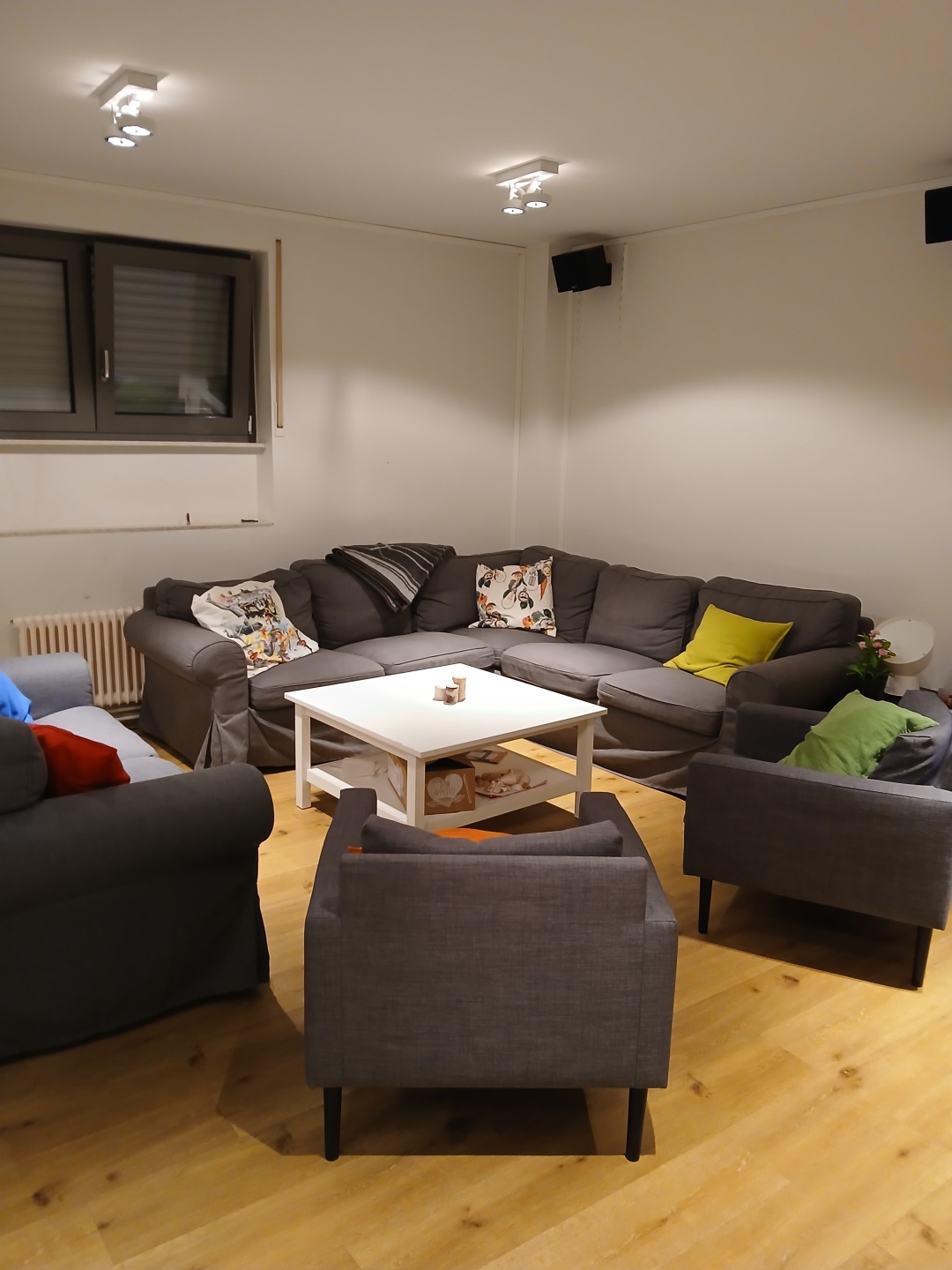 En esta habitación hay un sofá esquinero gris y tres sillones. Sobre ellos hay muchos cojines de colores y una mesa blanca.