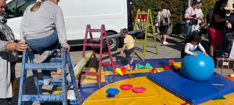 Los niños juegan en un colorido parque infantil Unos niños juegan en una colorida zona de juegos con escaleras, colchonetas y una gran pelota de ejercicios azul en una fiesta al aire libre