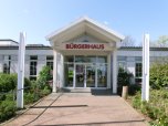 Entrada al centro comunitario de Niederroden con fachada de cristal y letras rojas "BÜRGERHAUS" sobre la puerta
