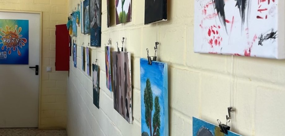 Obras de arte de JugendArt cuelgan de una pared blanca en un pasillo, incluido un retrato de una mujer con el pelo negro y un fondo rojo