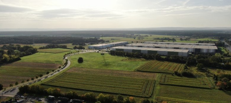 Vista aérea del polígono industrial VGP-Park Rodgau con grandes almacenes y terrenos agrícolas circundantes bajo un cielo nublado.