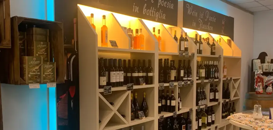 Etagère avec différentes bouteilles de vin et de spiritueux, surmontée de deux panneaux avec les textes 'Le vin est de la poésie en bouteille' et 'Le vin est de la poésie en bottiglia'.