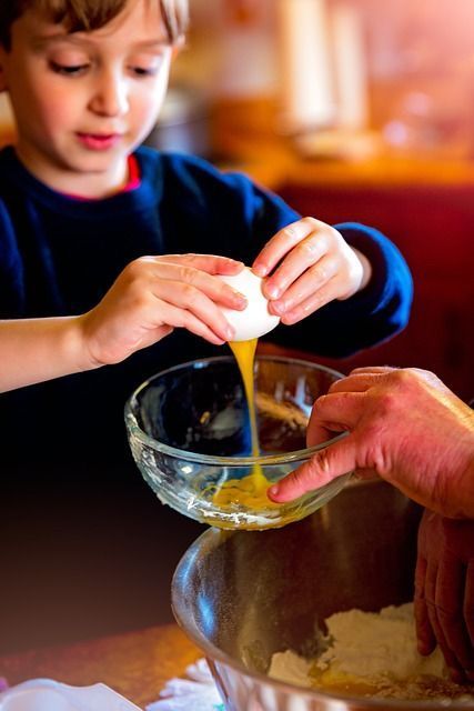 Un enfant casse un œuf et met le jaune et le blanc d'œuf dans un bol en verre.