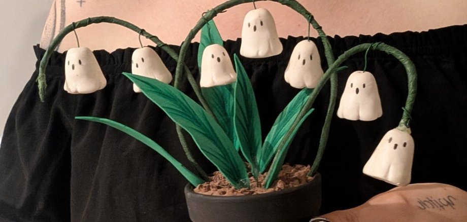 Atelier d'Halloween Une personne tient un petit pot de fleurs dont les feuilles vertes sont ornées de figures blanches aux formes fantomatiques, qui font penser à de petits fantômes