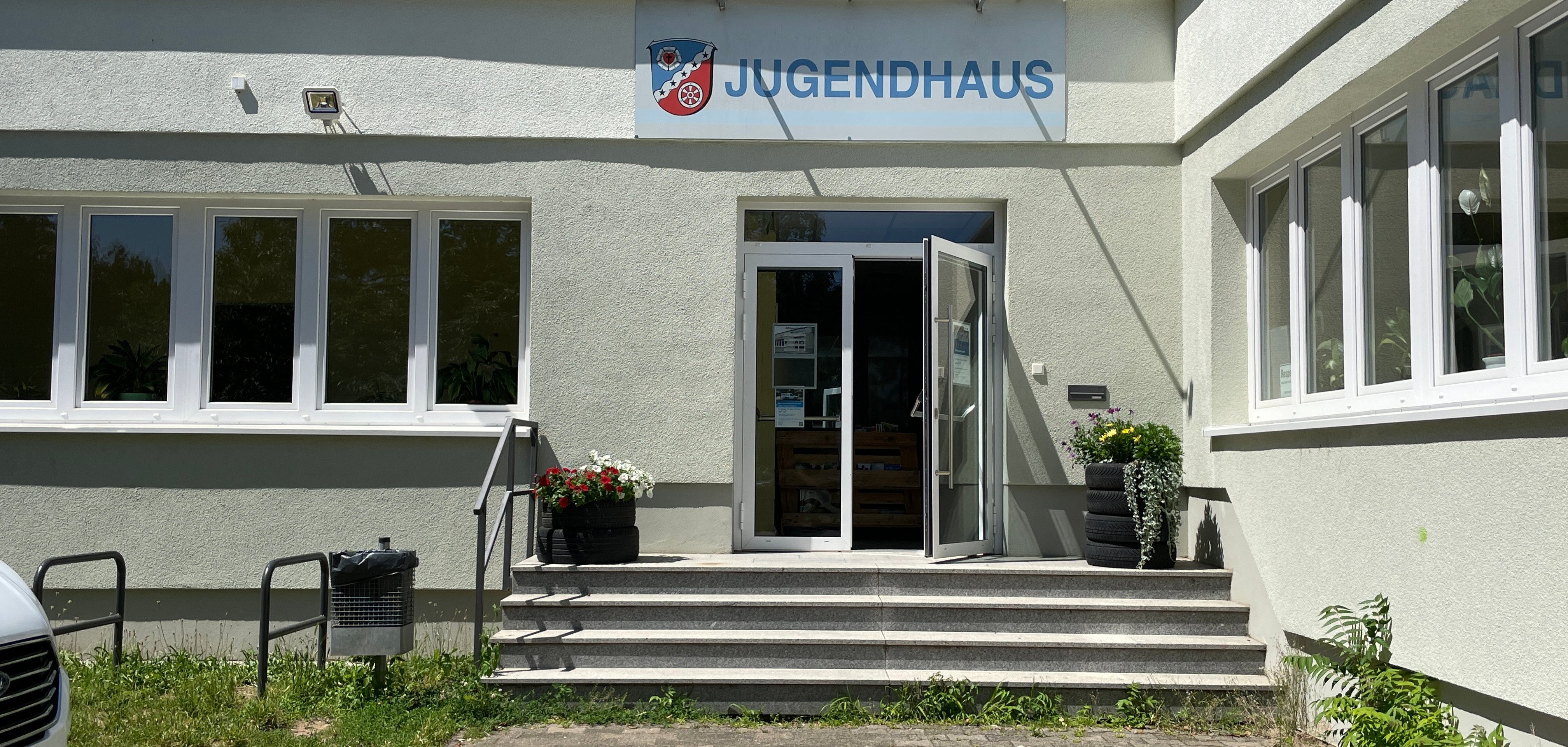 Le bâtiment de la maison des jeunes de Dudenhofen au niveau de l'entrée avec des marches et des supports à vélos sur la gauche.