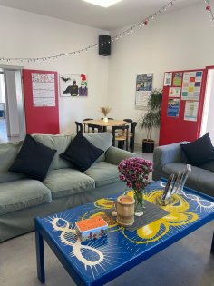 Au premier plan, deux canapés devant une table sur laquelle sont posées des fleurs. En arrière-plan, une table avec des chaises.