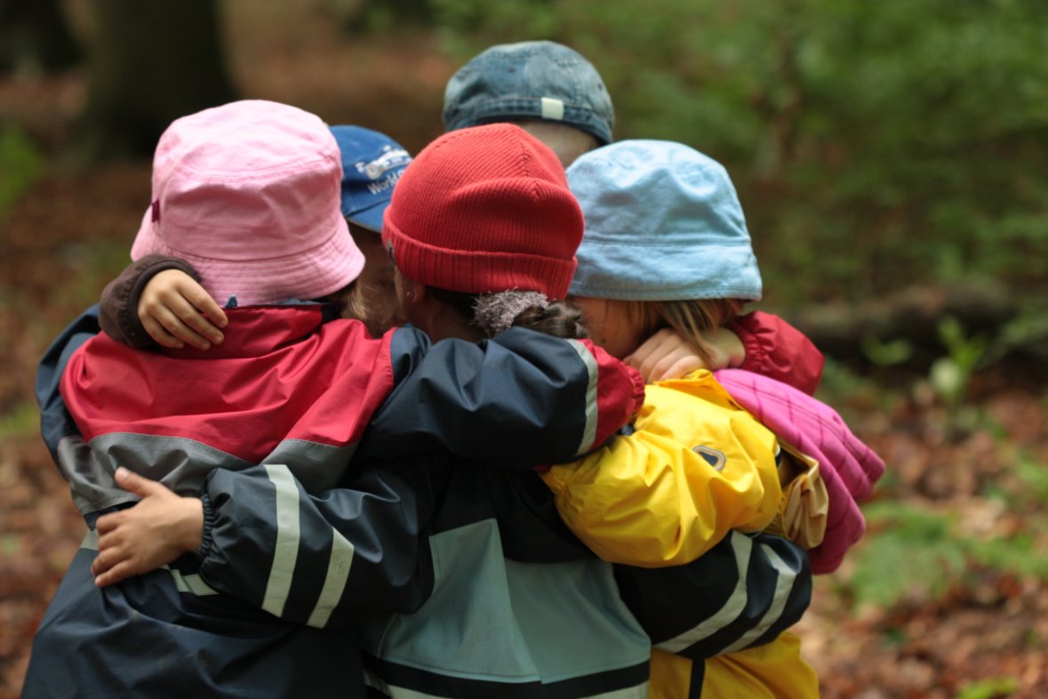 Quatre enfants dans la forêt Quatre enfants portant des vestes et des bonnets colorés s'enlacent dans la forêt